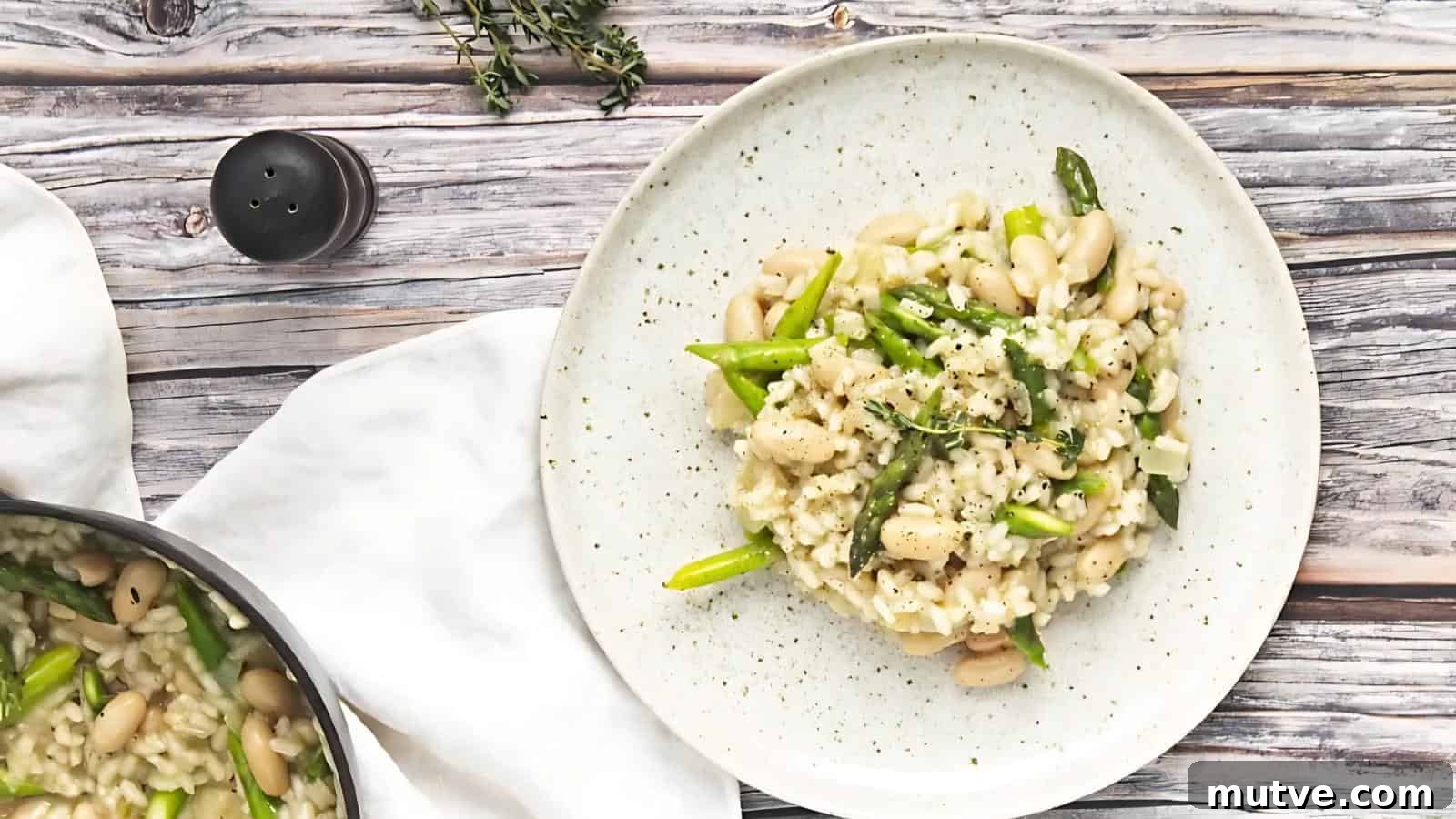 40 End-of-Summer Cookout Recipes to Celebrate Summer's Finale 35 A plate of creamy risotto with white beans and asparagus on a speckled dish, set on a wooden table with herbs and a pepper shaker nearby.