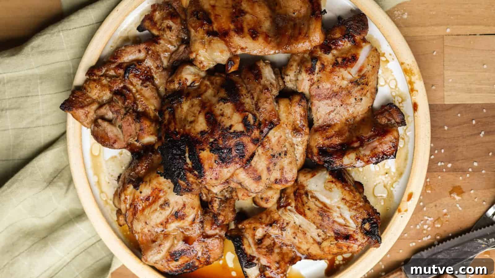 40 End-of-Summer Cookout Recipes to Celebrate Summer's Finale 36 A plate of grilled chicken thighs on a round dish, placed on a wooden surface with a green cloth and scattered salt nearby.