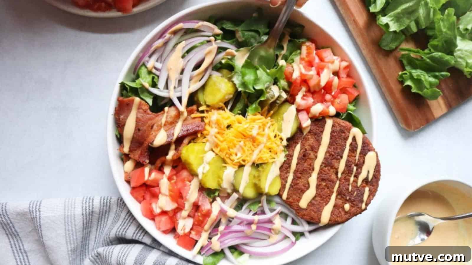 40 End-of-Summer Cookout Recipes to Celebrate Summer's Finale 37 A salad bowl with lettuce, tomato, red onion, pickles, shredded cheese, bacon, a burger patty, and dressing, viewed from above.