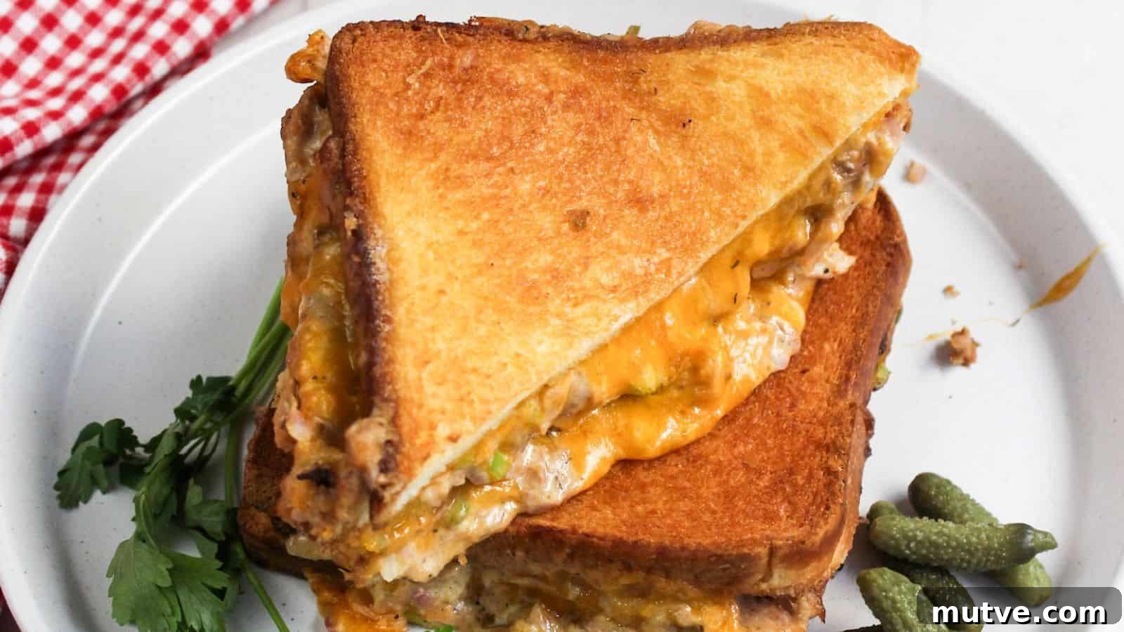 40 End-of-Summer Cookout Recipes to Celebrate Summer's Finale 5 A grilled cheese tuna sandwich on a plate, cut in half, with melted cheese and fillings visible, accompanied by pickles and parsley.