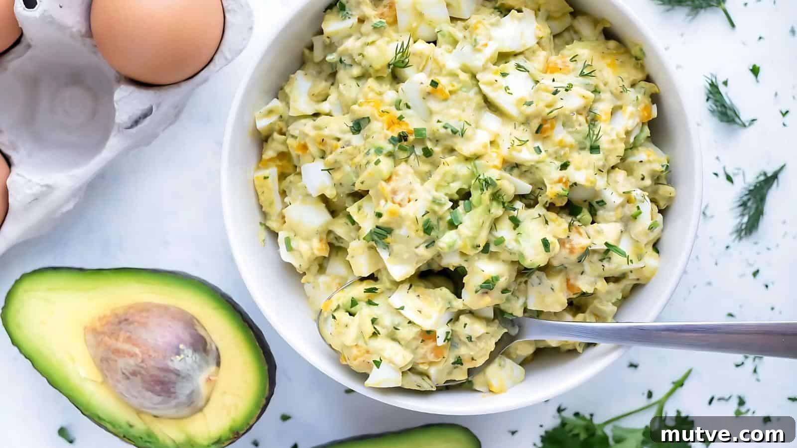 40 End-of-Summer Cookout Recipes to Celebrate Summer's Finale 41 A bowl of egg salad garnished with herbs sits on a white surface near avocado halves, eggs, and fresh herbs, with a spoon in the bowl.