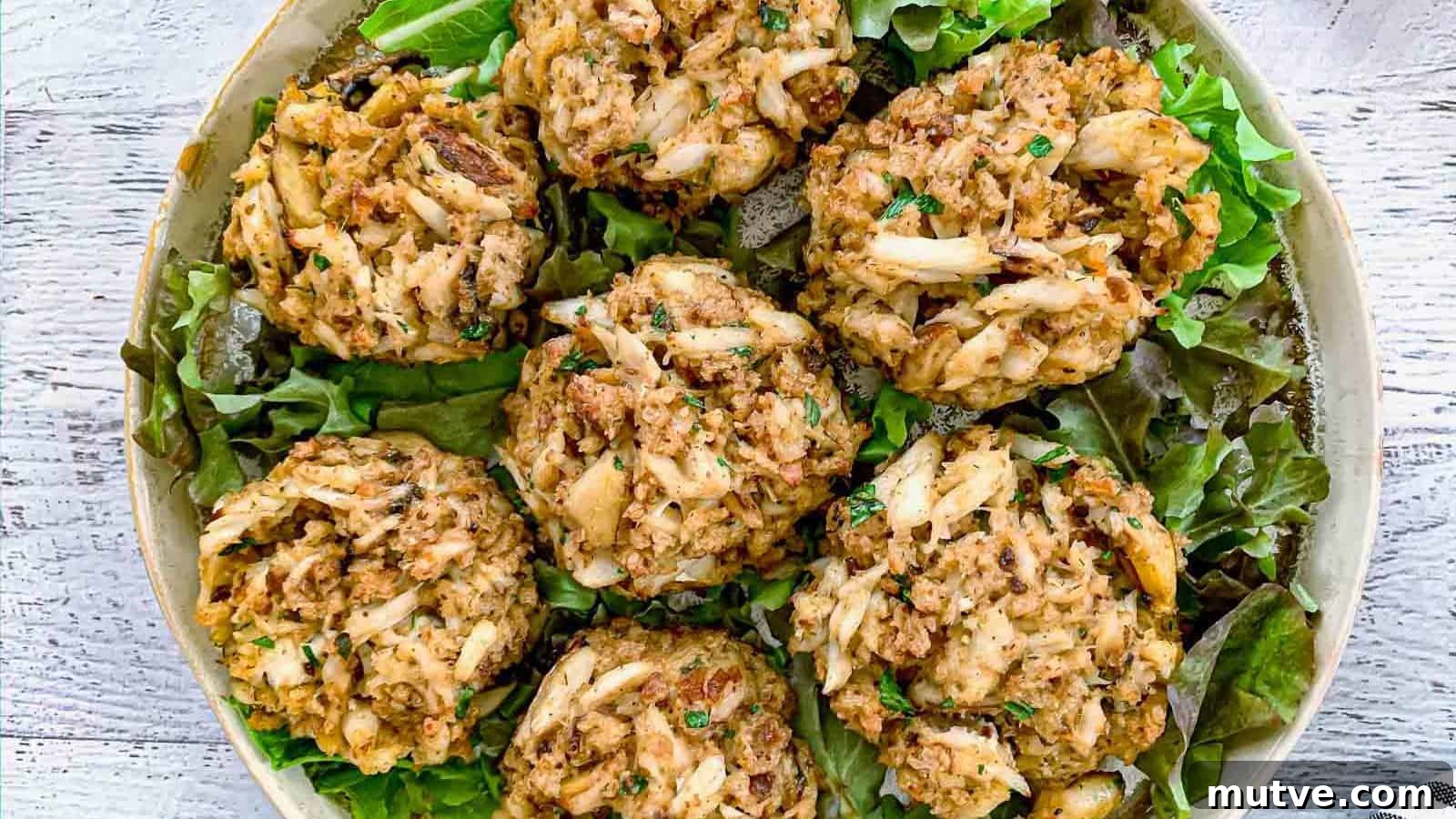 40 End-of-Summer Cookout Recipes to Celebrate Summer's Finale 42 A plate of six crab cakes sits on a bed of leafy greens, displayed on a light-colored surface.