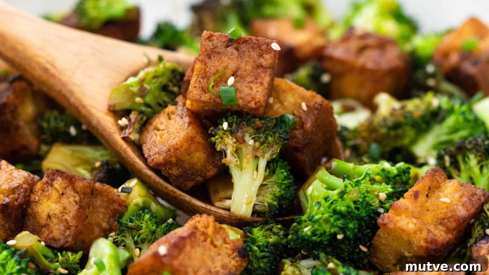 40 End-of-Summer Cookout Recipes to Celebrate Summer's Finale 8 Close-up of roasted broccoli and tofu cubes tossed with sesame seeds in a wooden spoon, set against a blurred background.