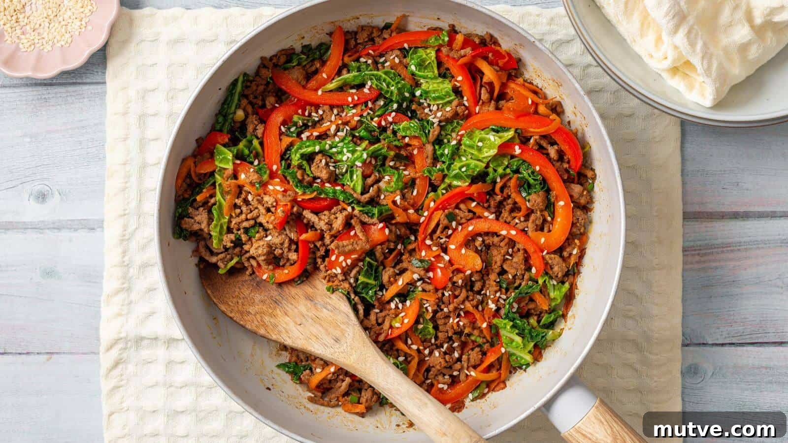 40 End-of-Summer Cookout Recipes to Celebrate Summer's Finale 9 A skillet filled with a colorful stir-fry of ground meat, bell peppers, leafy greens, and sesame seeds, with a wooden spoon resting in it. Plates and a stack of flatbreads are nearby.