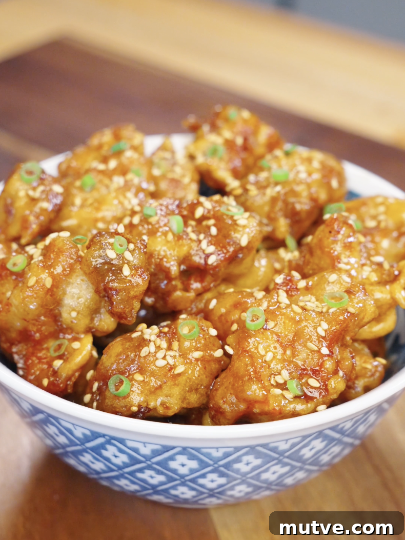 Bowl filled with crispy honey butter fried chicken pieces coated in a sticky glaze and topped with sesame seeds and scallions.