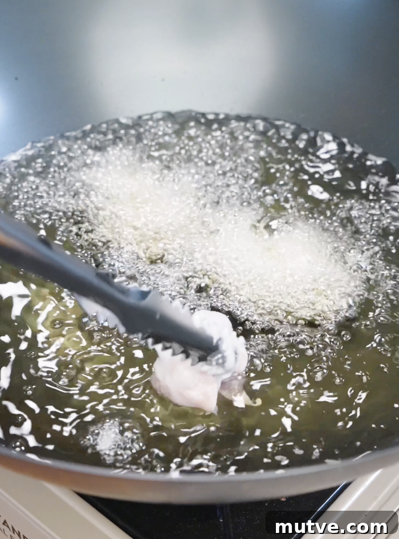 Battered chicken pieces being lowered into hot oil, frying until golden and crispy for the Honey Butter Fried Chicken Recipe.