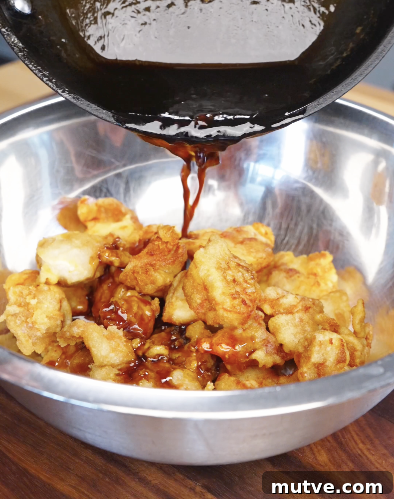 Thick honey butter sauce being poured over crispy fried chicken in a bowl, coating each piece evenly.