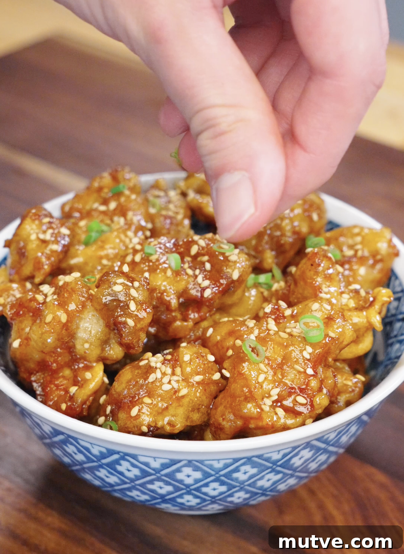 Hand sprinkling sesame seeds and chopped scallions over freshly glazed honey butter fried chicken in a bowl.