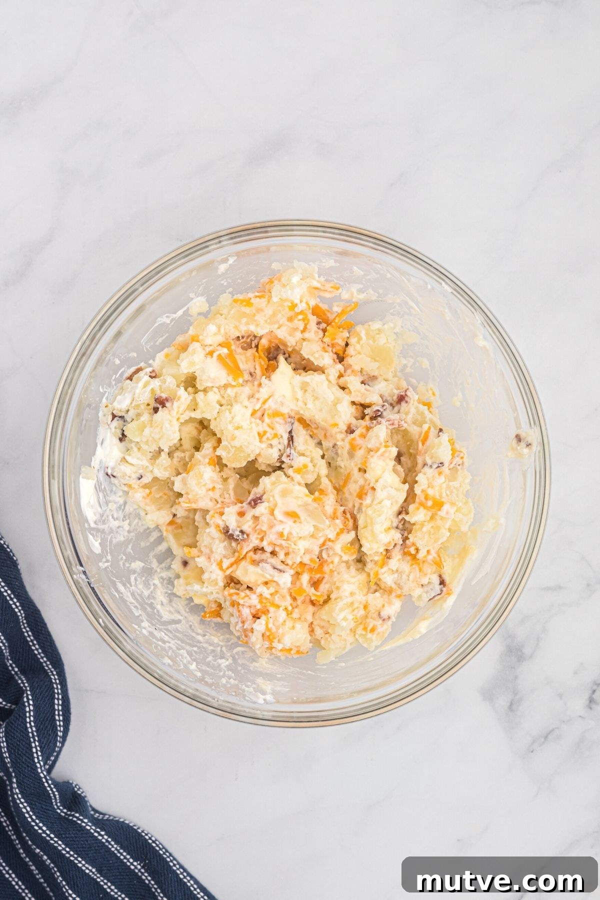 Potato mixed with cheese, sour cream and bacon in a mixing bowl. 