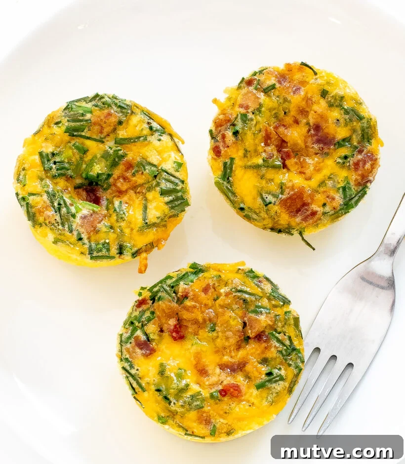 Bacon and Egg Breakfast Muffins Recipe 2 Three bacon egg muffins on a white plate with a silver fork.