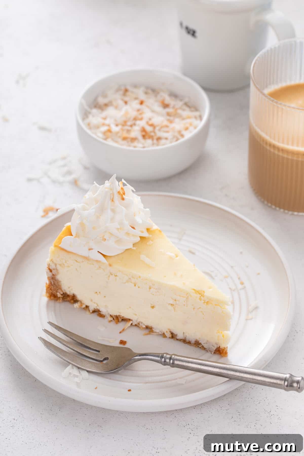 Creamy Coconut Cheesecake Recipe 2 Slice of coconut cheesecake next to a fork on a white plate.