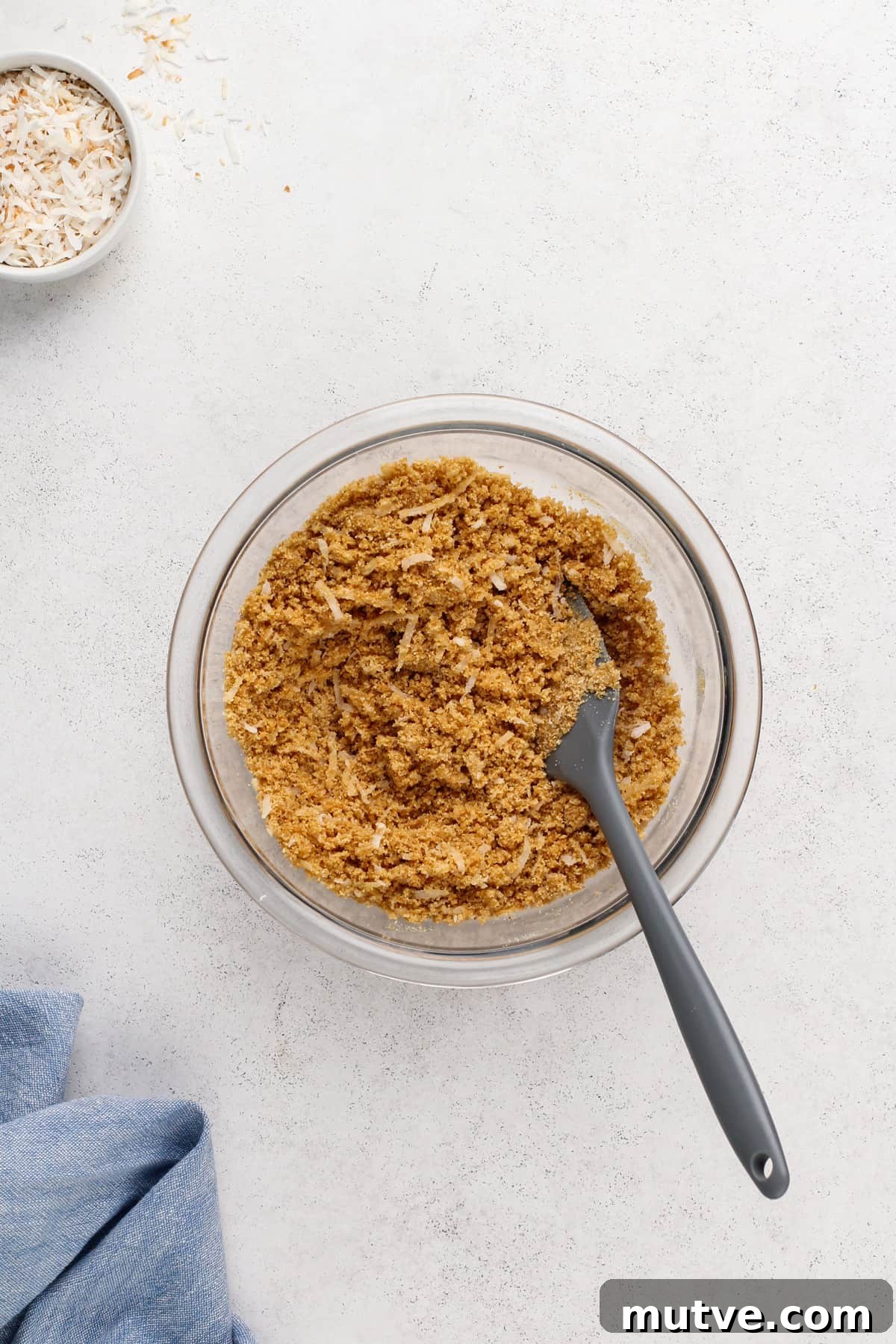 Creamy Coconut Cheesecake Recipe 6 Graham cracker crumbs and coconut mixed with melted butter in a glass mixing bowl.