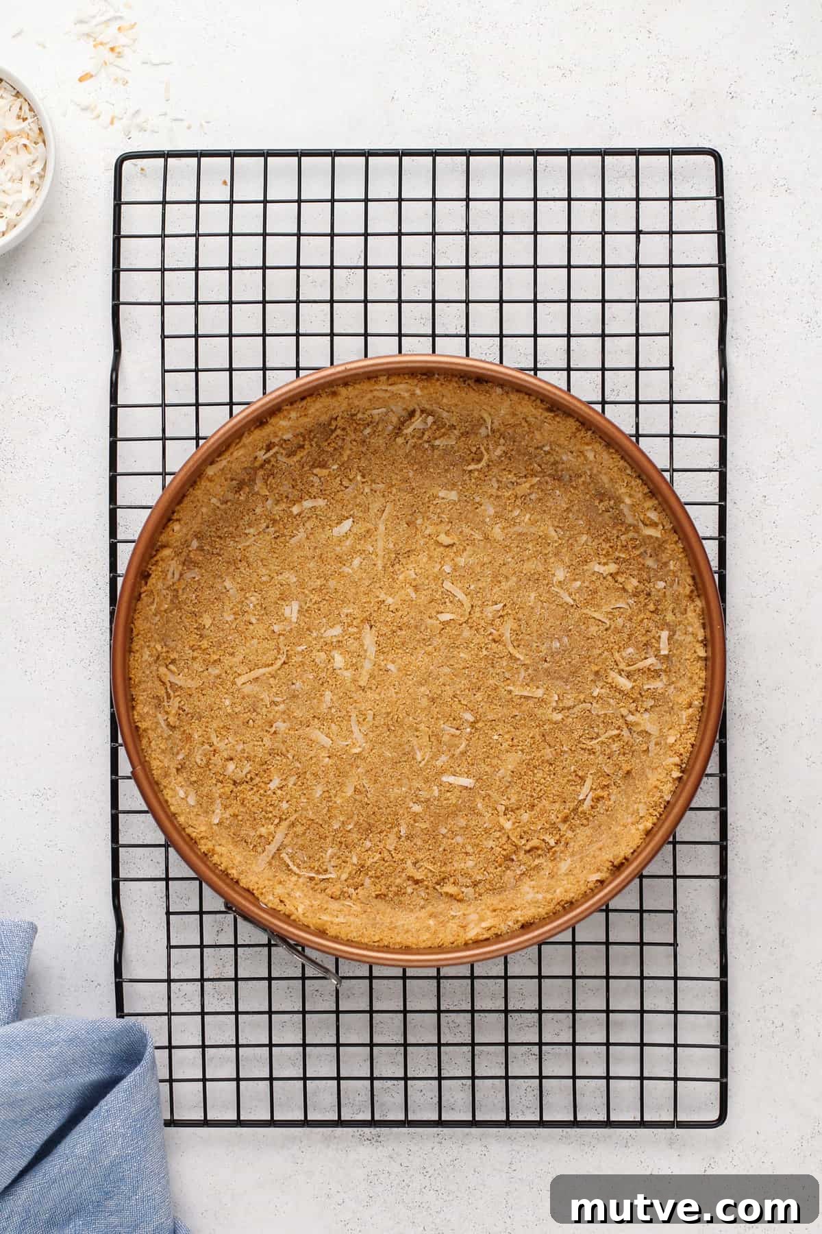 Creamy Coconut Cheesecake Recipe 7 Baked coconut graham cracker crust in a springform pan set on a wire rack.