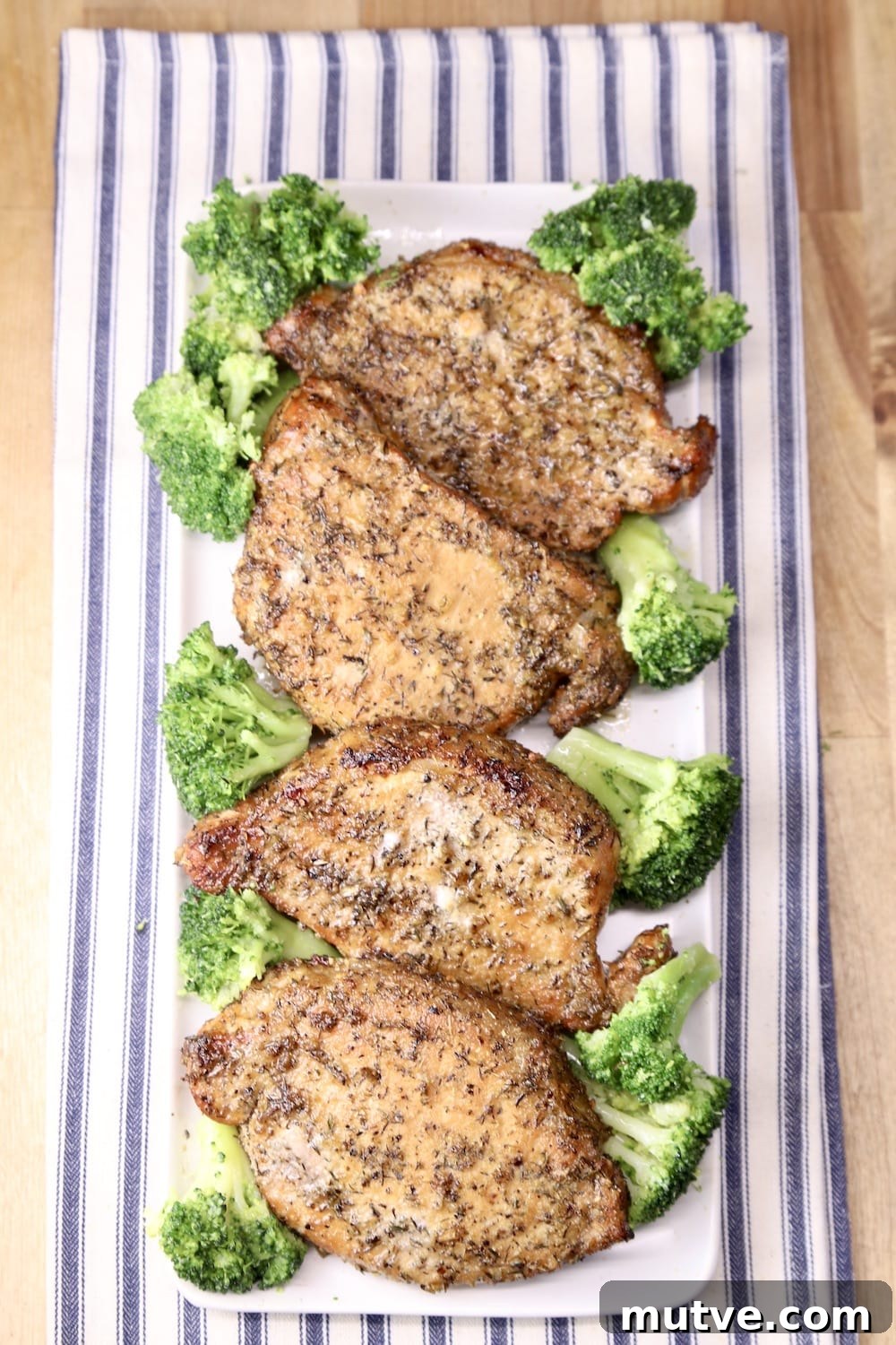 4 grilled pork chops with broccoli on a rectangle platter, blue stripe towel under platter