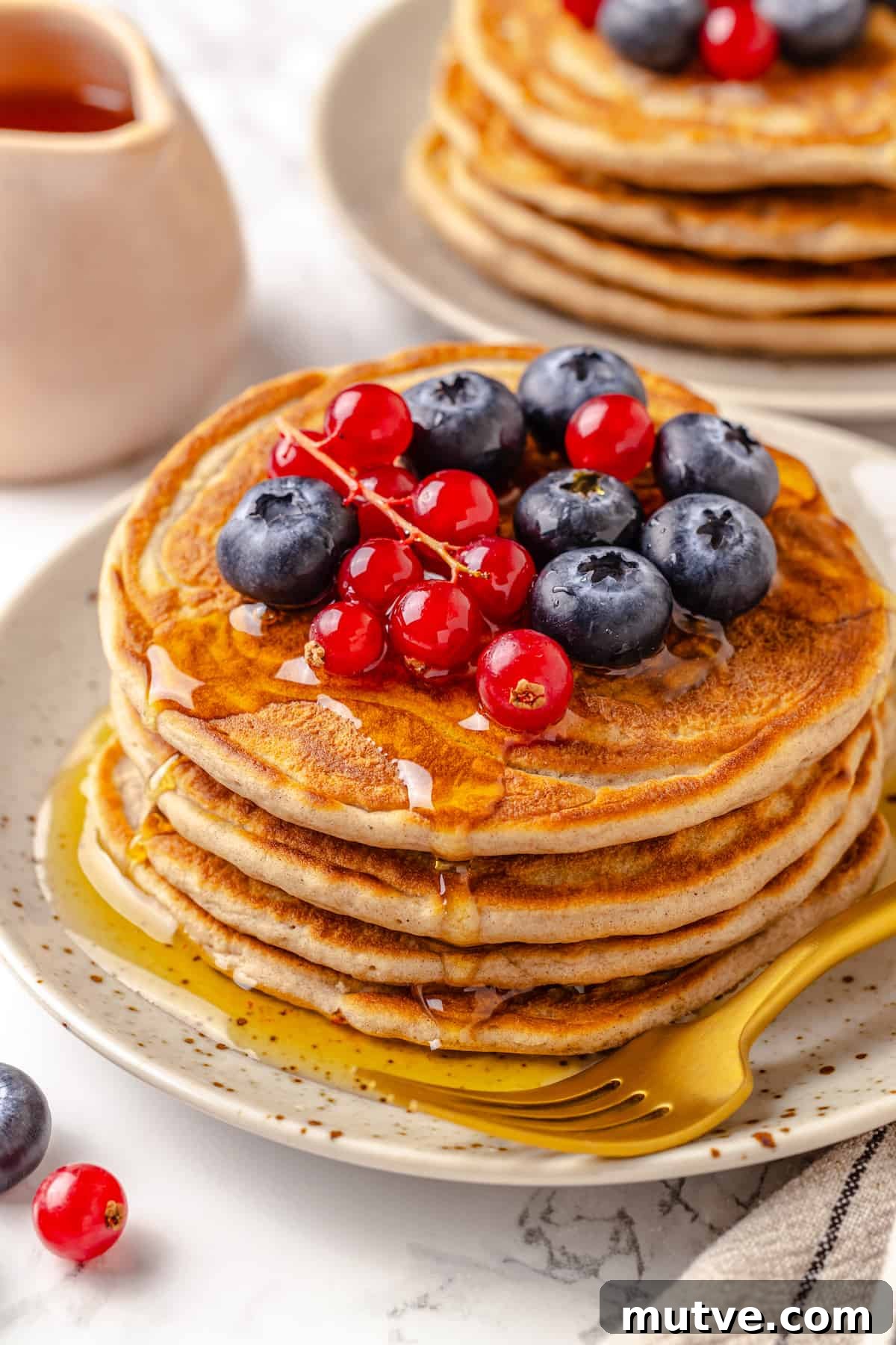 Stack of 4 protein pancakes on plate with maple syrup and berries