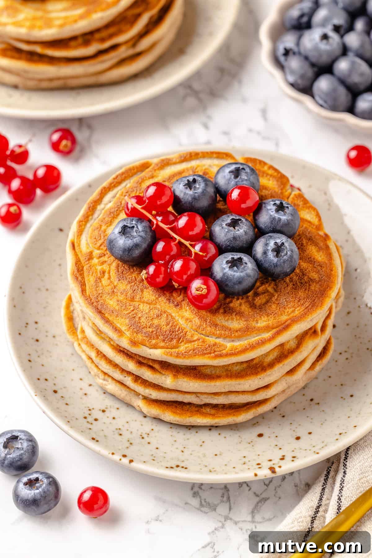 Stack of protein pancakes on plate with fresh berries on top