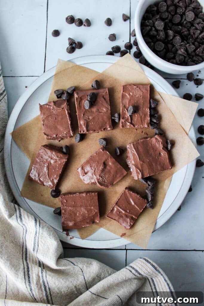 High-Protein Cottage Cheese Fudge - 4-Ingredient Recipe 2 A plate of pieces of cottage cheese fudge on parchment paper with chocolate chips in the background.