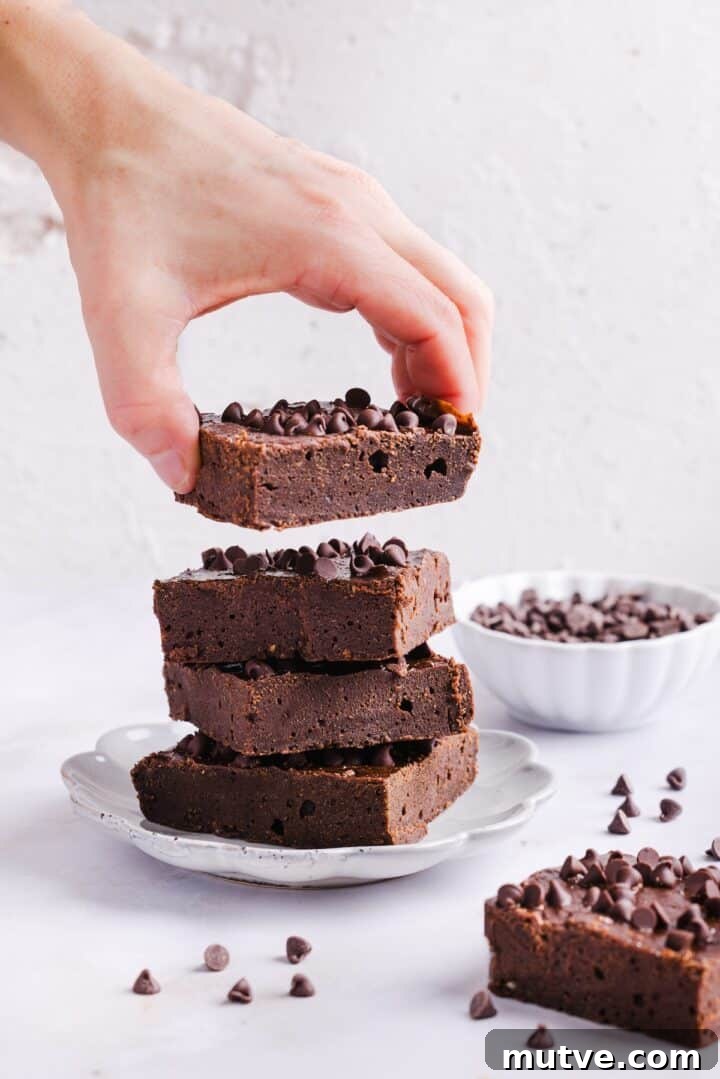 Cottage Cheese Brownies Recipe: Moist, Protein-Packed Treat 3 Woman's hand grabbing a cottage cheese brownie from a stack of brownies on a plate