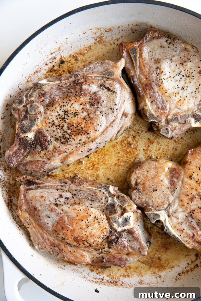 One-Pan Smothered Pork Chops with Mushroom Gravy 3 Pork chops searing in a hot skillet with melted butter and olive oil.