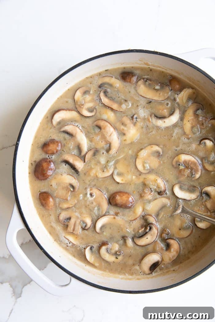 One-Pan Smothered Pork Chops with Mushroom Gravy 4 White ceramic Dutch oven filled with cooked onions and mushrooms in a sauce made with flour and chicken broth.