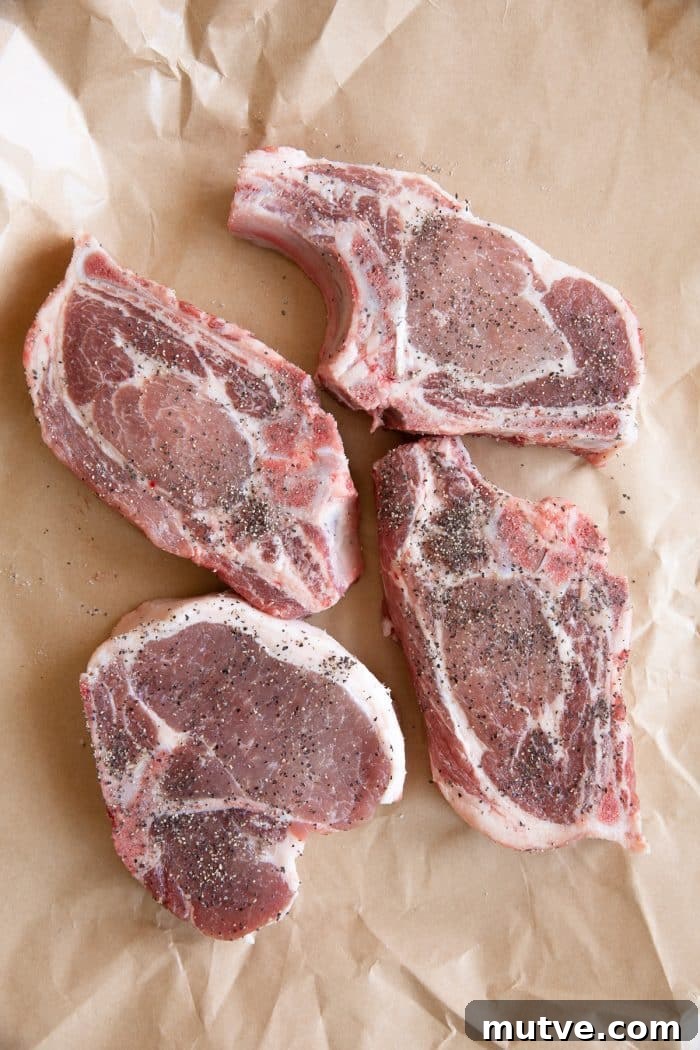 Four thick-cut pork chops seasoned with salt, pepper, and spices on butcher paper.