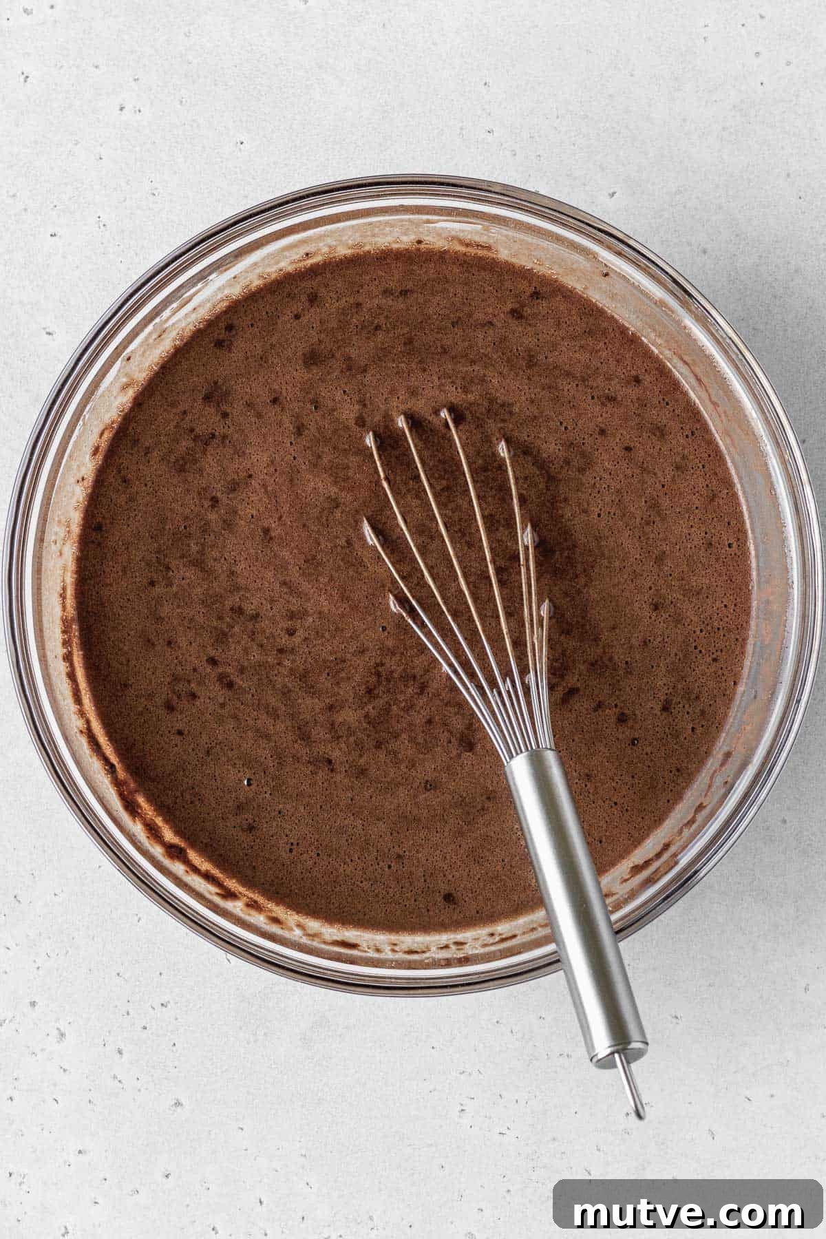 Gluten-free German chocolate cake batter in a glass bowl with a whisk inside.