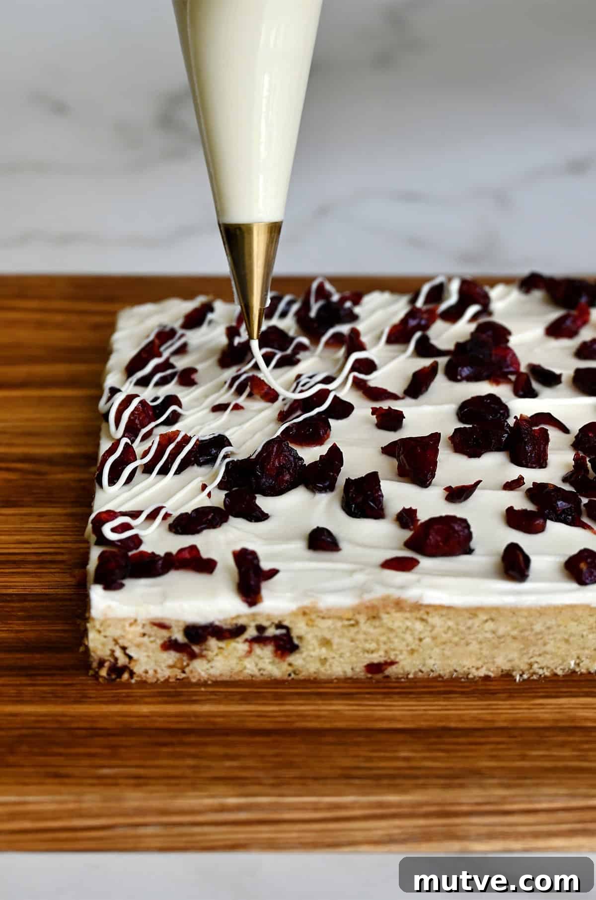 Piping melted white chocolate in a zigzag over cranberry bliss bars.