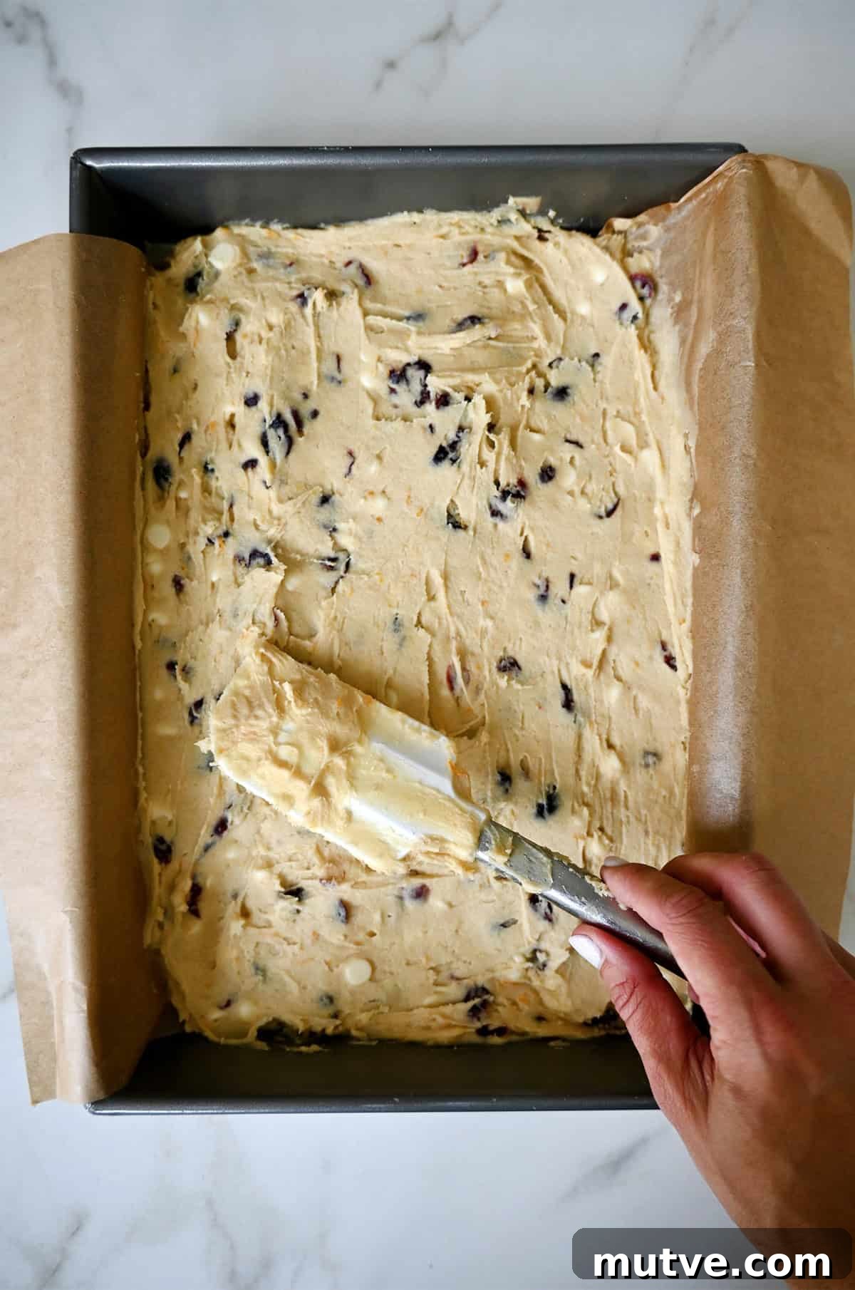 Spreading cranberry bliss blondie batter into a parchment paper-lined 9x13 baking pan.