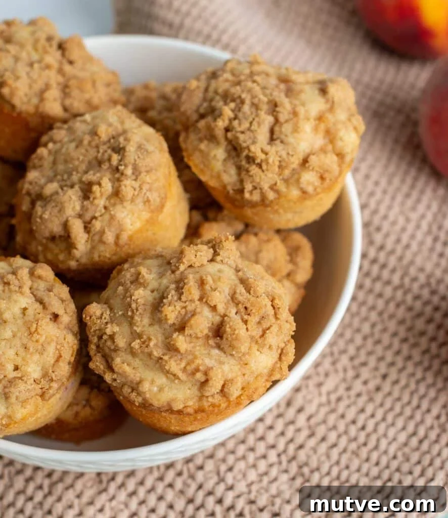 Moist Sourdough Peach Muffins Recipe 2 A bowl full of homemade sourdough peach muffins with a crumb topping.