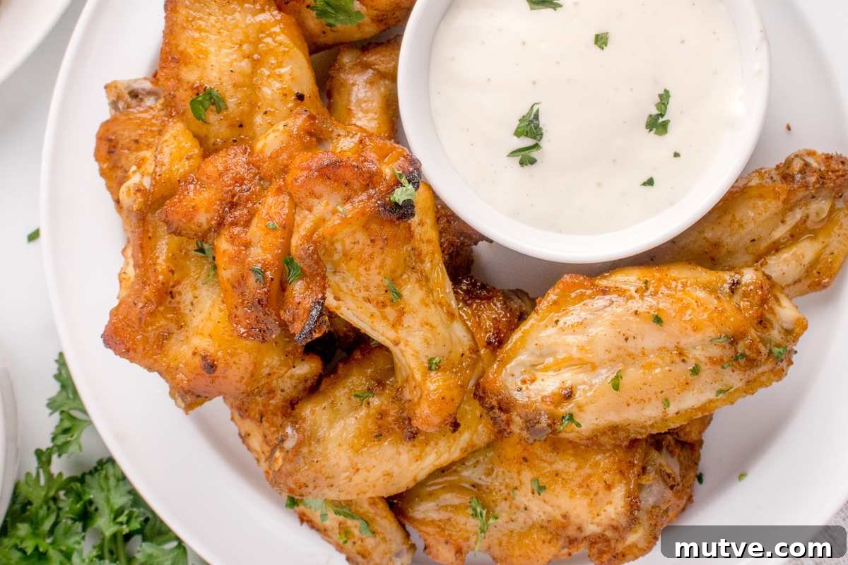 Extra Crispy Oven-Baked Chicken Wings Recipe 8 chicken wings on plate with bowl of ranch dressing.