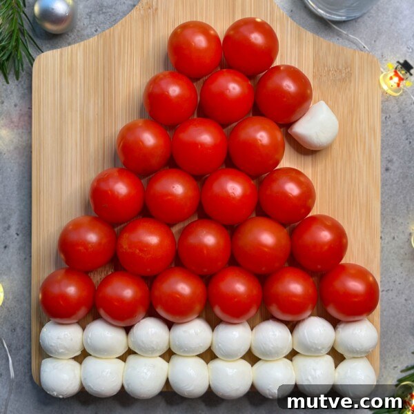 A Santa hat shape made from rows of cherry tomatoes and mozzarella balls on a wooden board.