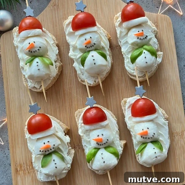 Six slices of bread topped with cream cheese, shaped like snowmen using cherry tomatoes for hats and veggies for details—these festive bites make delightful Christmas Party Appetizers, beautifully arranged on a wooden board.