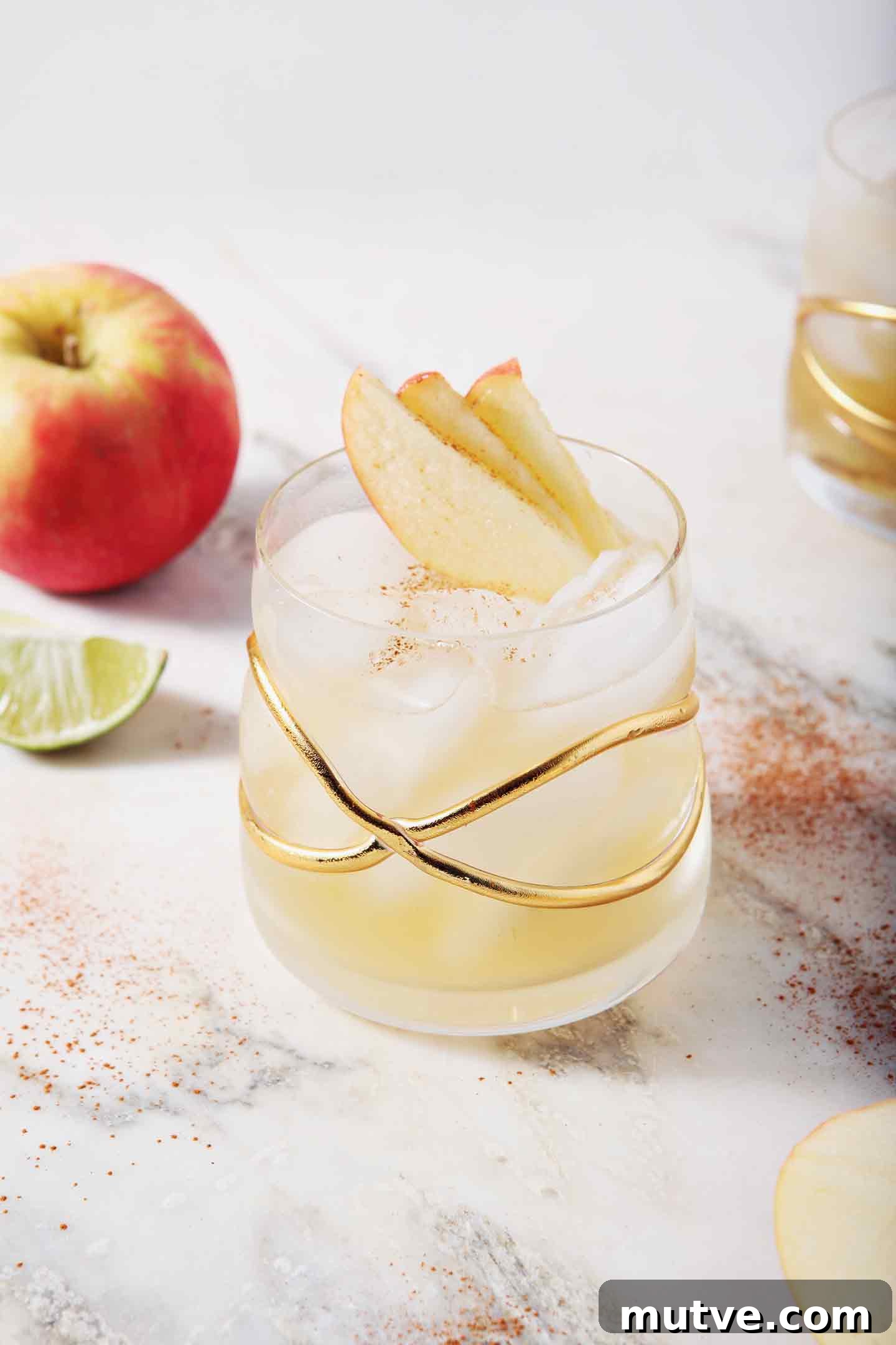 Apple Cider Moscow Mule Cocktail Recipe 2 Two Apple Cider Moscow Mules sit on a marble background, surrounded by apples, lime slices and cinnamon