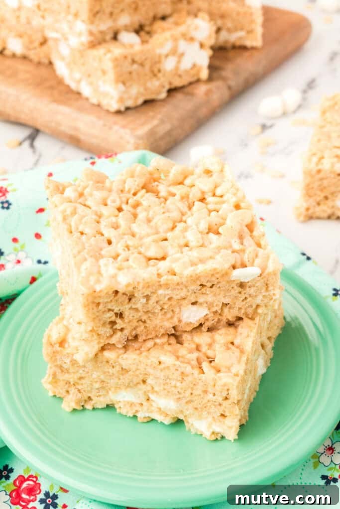 Browned Butter Rice Krispie Treats 2 Two stacked Browned Butter Rice Crispy Treats on a green plate with more bars in the background on a wooden board.