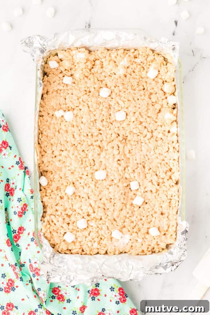 Browned Butter Rice Krispie Treats 12 Browned Butter Rice Crispy Treats pressed into a foil-lined pan, cooling before cutting into squares.