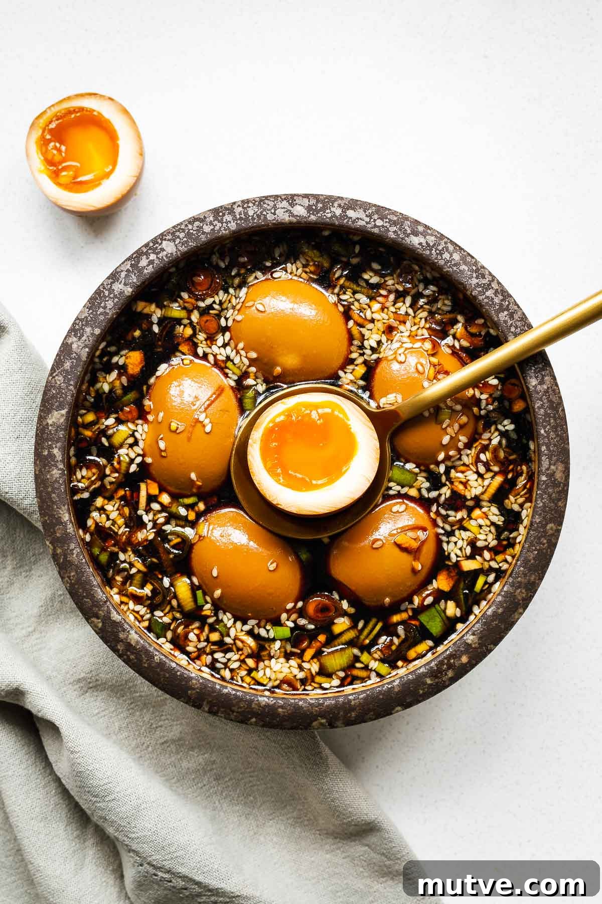 Mayak Eggs Recipe: Korean Soy-Marinated Ramen Eggs 2 Mayak eggs in a ceramic bowl with one egg sliced in half to show the jammy egg centre.
