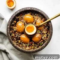 Mayak Eggs Recipe: Korean Soy-Marinated Ramen Eggs 13 Mayak eggs in a ceramic bowl with one egg sliced in half to show the jammy egg centre.
