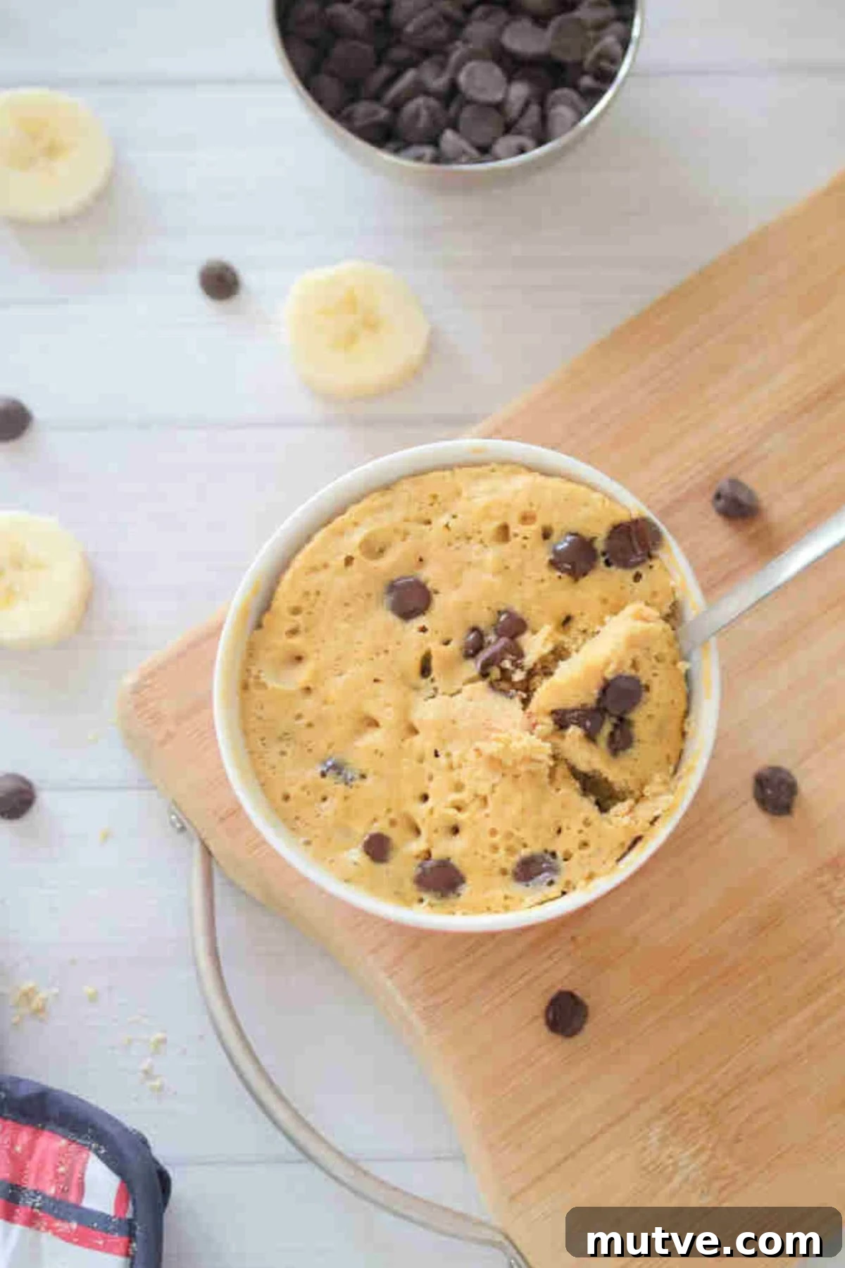 3-Ingredient Dairy-Free Protein Mug Cake 2 Mug cake with chocolate chips in a red bowl with a spoon in it on a cutting board.