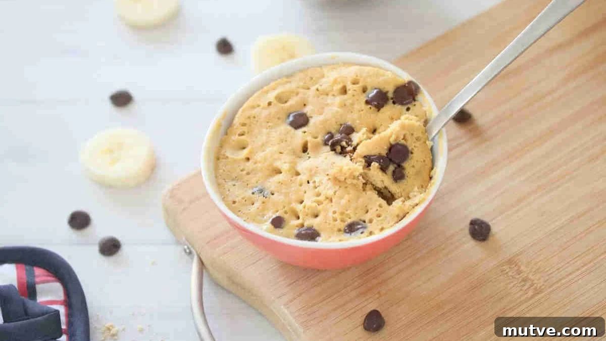 3-Ingredient Dairy-Free Protein Mug Cake 11 Mug cake with chocolate chips in a red bowl with a spoon in it on a cutting board.