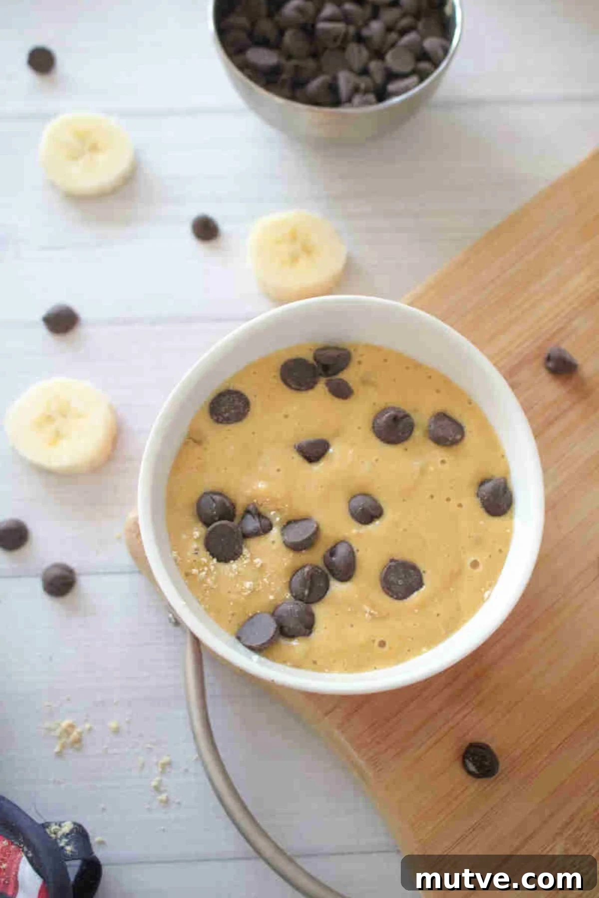 3-Ingredient Dairy-Free Protein Mug Cake 7 Raw mug cake in a bowl with chocolate chips on top with the bowl on a cutting board.