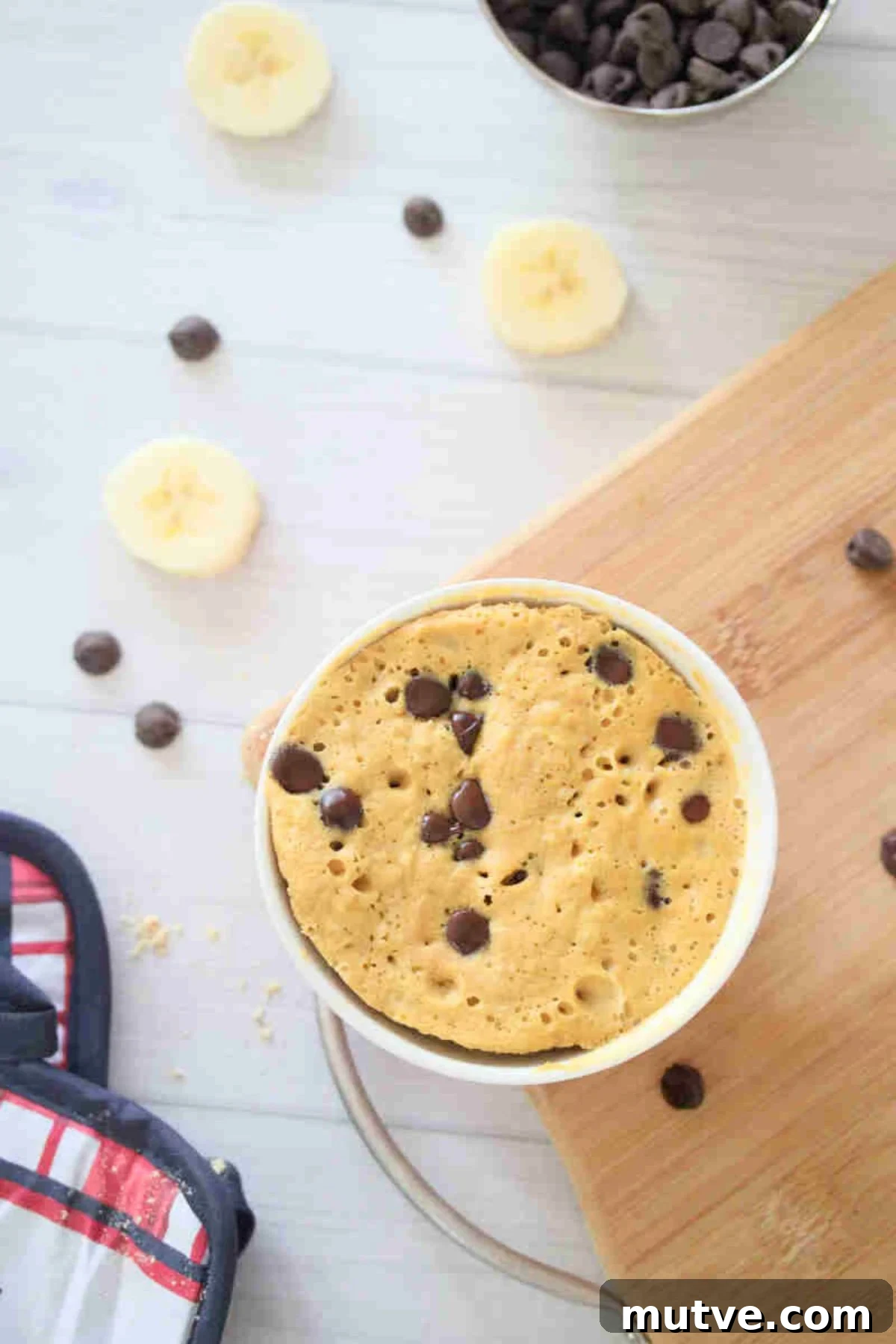 3-Ingredient Dairy-Free Protein Mug Cake 9 Mug cake with chocolate chips in a red bowl on a cutting board.