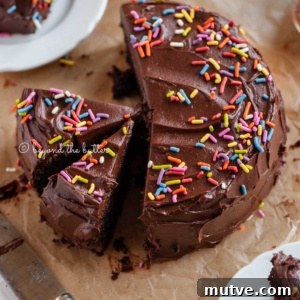 Moist Single-Layer Chocolate Cake Recipe 13 Angled image of sliced single layer chocolate cake on parchment paper with slices of cake on small dessert plates around it and a knife on parchment paper.