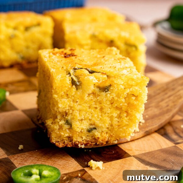 A serving utensil holds a piece of jalapeno cheddar cornbread on top of a wooden cutting board for serving.