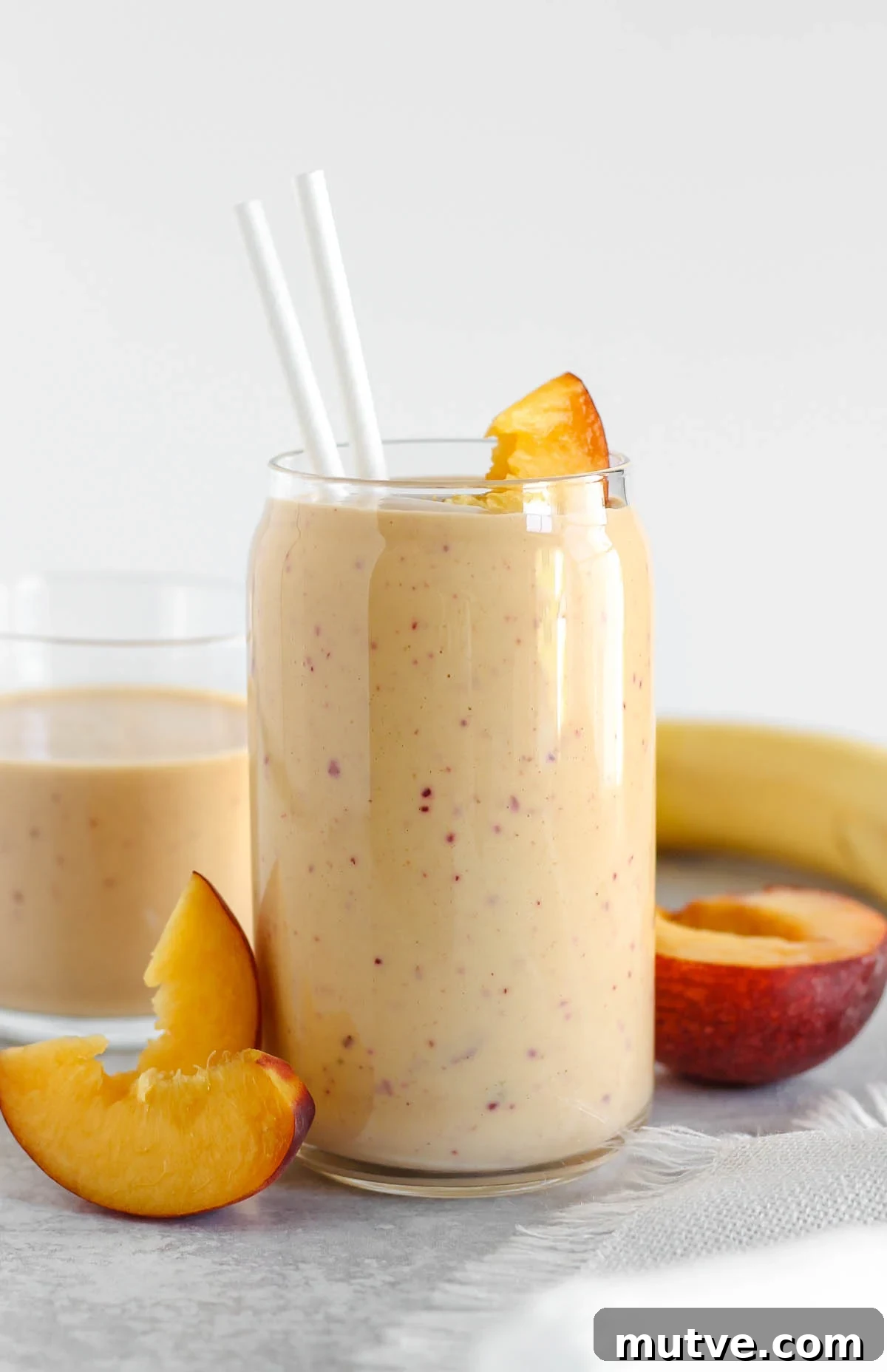 Tall glass filled with peach smoothie with sliced peaches leaning up against the glass.