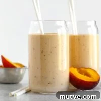 Two glasses filled with peach smoothie with half a peach laying next to the glasses.