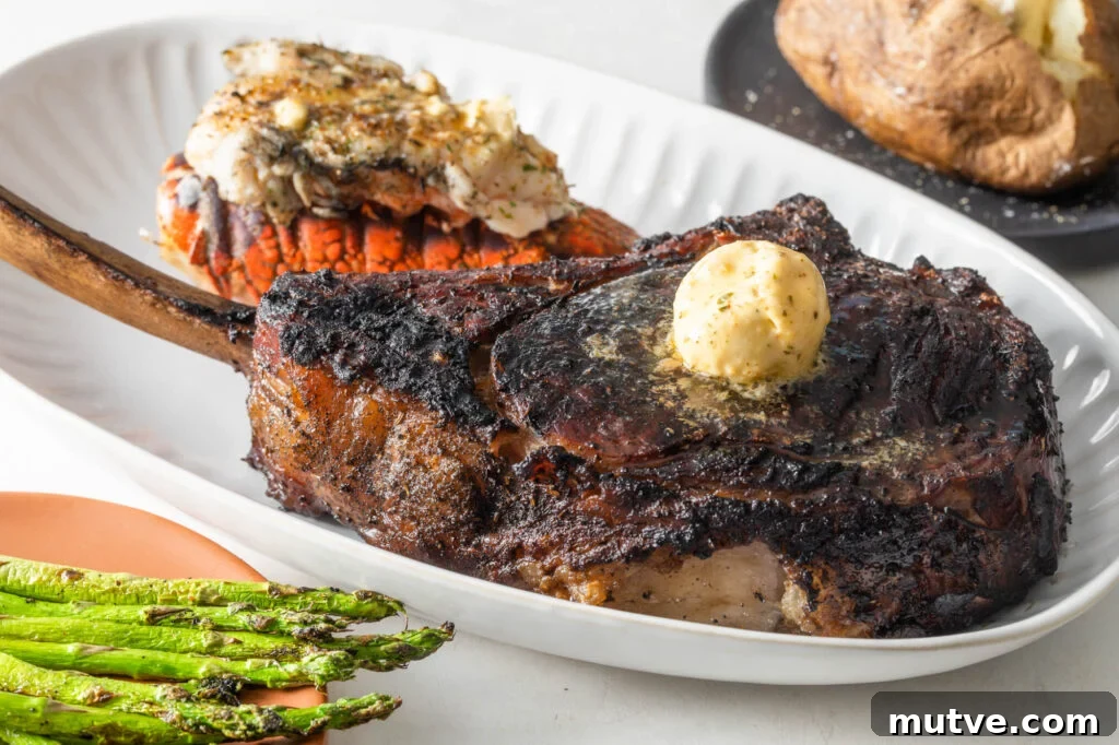 cooked tomahawk steak topped with a scoop of compound butter on a plate with a cooked lobster tail. asparagus spears and a baked potato with butter in the background