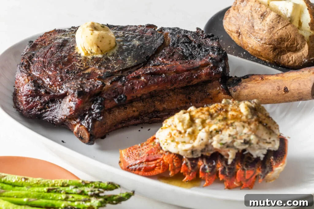 cooked tomahawk steak topped with a scoop of compound butter on a plate with a cooked lobster tail. asparagus spears and a baked potato with butter in the background