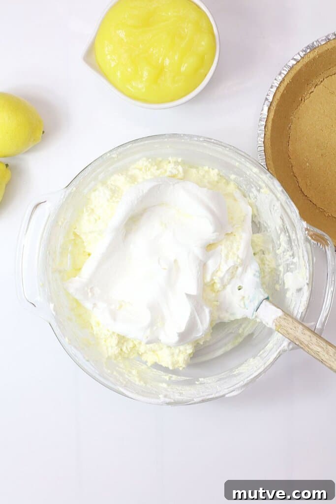 cool whip being added to pie filling in a glass bowl.