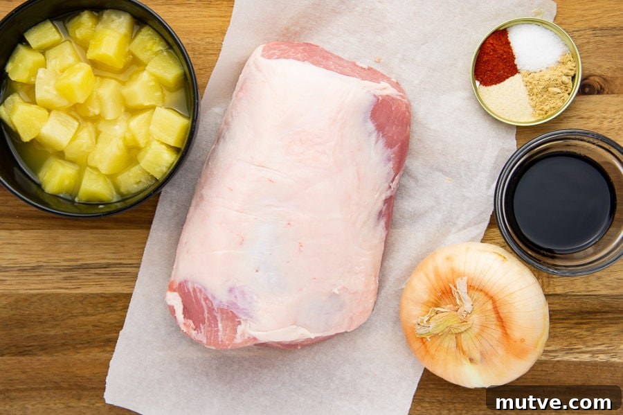 a pork loin on a piece of parchment paper with a bowl of pineapple chunks, an onion, soy sauce, and a spice mix